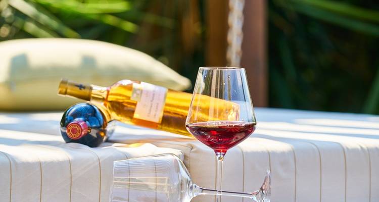 Elegant setup with a bottle of white wine and a glass of red resting on a striped lounger.