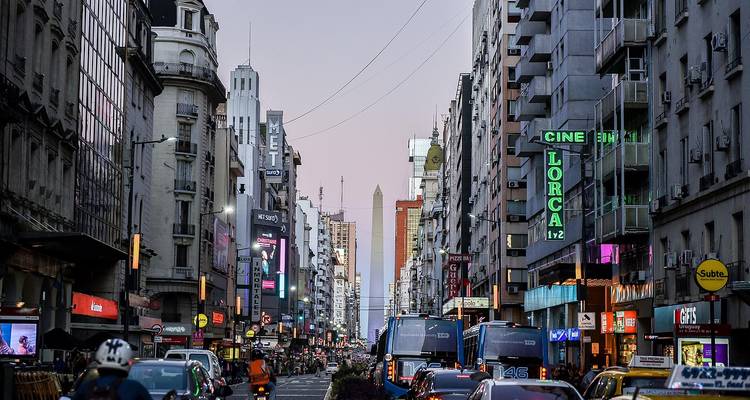 Evening view down illuminated city street toward the Obelisk with neon signs and traffic.