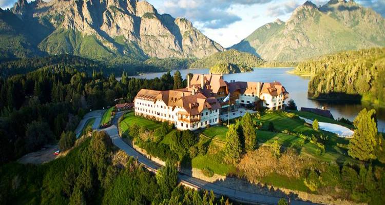 Aerial view of Llao Llao Hotel perched on a green peninsula surrounded by lakes and mountains.