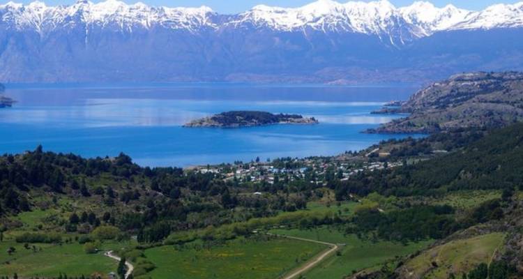 A turquoise lake set against snow-capped Andes with a small settlement on its shore.