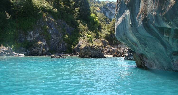 Crystal-clear turquoise water laps against dramatic marble walls and forested cliffs.