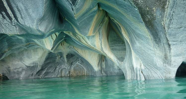 Inside the Marble Caves, swirling mineral patterns arch above emerald water.