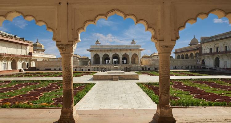 Uitzicht op een omsloten binnenplaats door uitgesneden bogen in het Agra Fort met geometrische tuinen onder blauwe lucht.