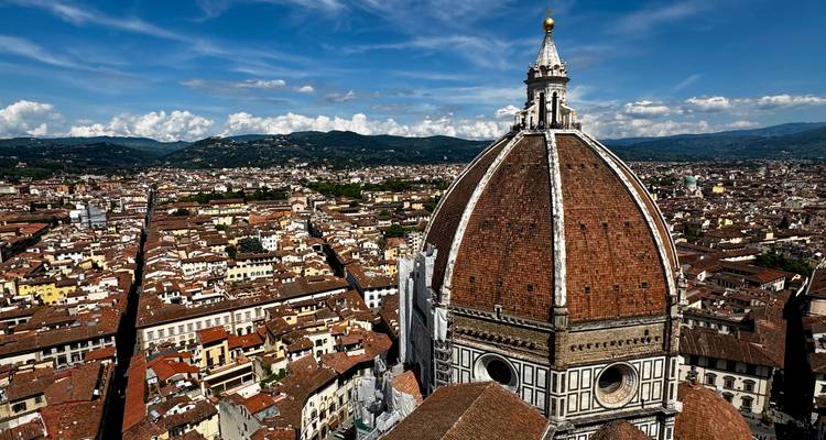 Iconic red-tiled dome rising above Florence's dense rooftops with distant hills under bright skies.