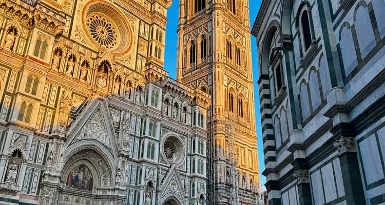 Close-up view of Florence’s cathedral façade and the Giotto bell tower glowing in warm light against a blue sky.