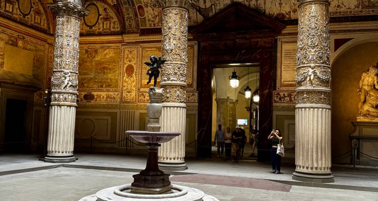 Ornate renaissance courtyard with carved columns, fountain, and visitors admiring the interior decor.