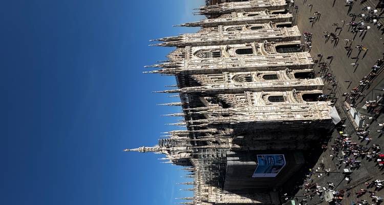 Aerial view of Milan Cathedral (Duomo di Milano) dominating the busy city square under a deep blue sky.