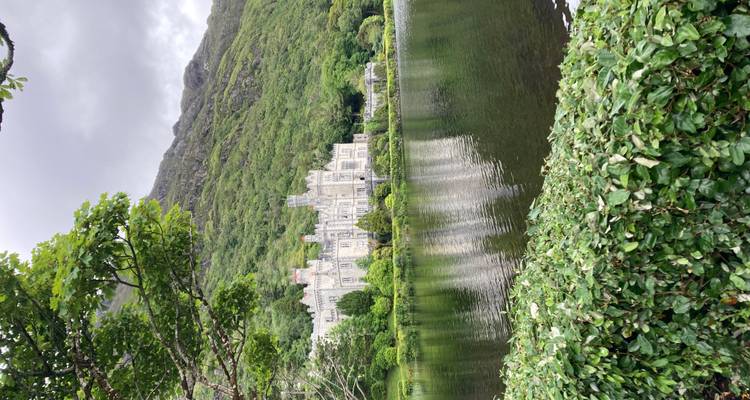 Neo-Gothic abbey reflected in a still lake framed by lush green mountains and trees.