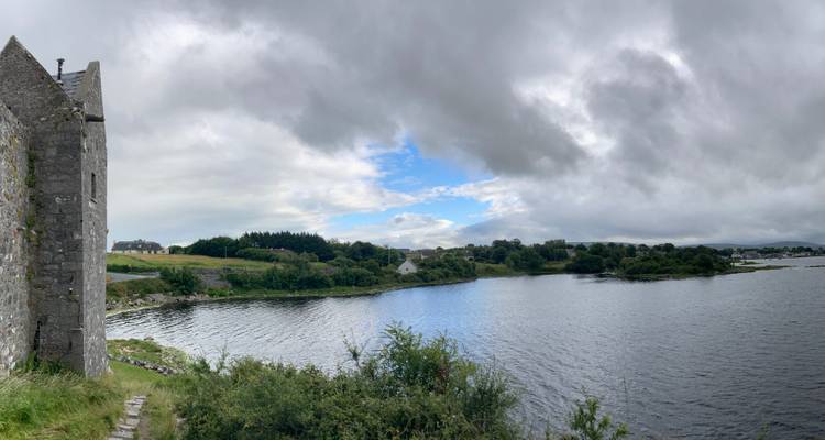 Stone castle ruin on a lakeshore with panoramic view of calm water and patchy clouds above.