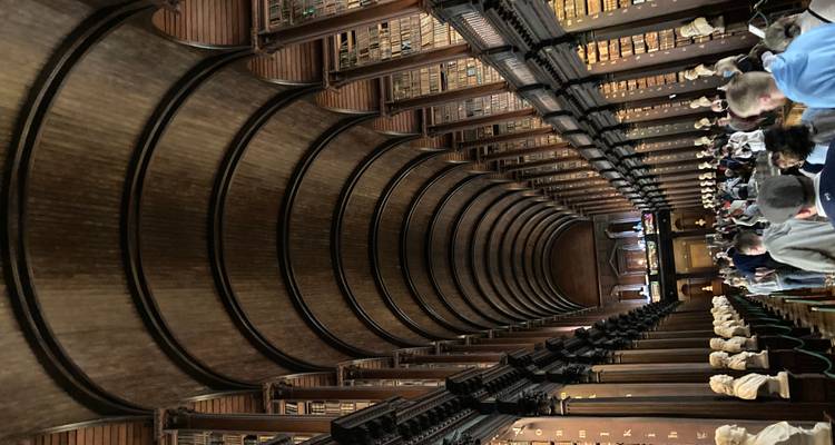 Grand vaulted library hall lined with book-filled shelves and marble busts crowded with visitors.