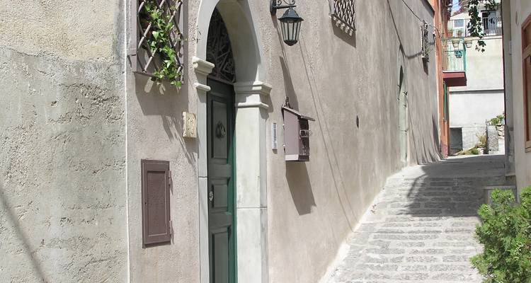 Ruelle étroite et silencieuse pavée de pierre avec une porte en bois vert et une entrée voûtée baignée de lumière vive.