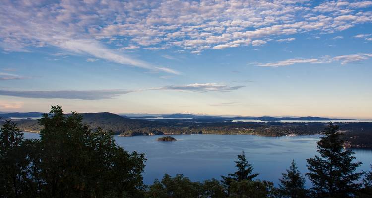 High viewpoint over a broad bay dotted with islands and bordered by wooded hills under a blue sky.