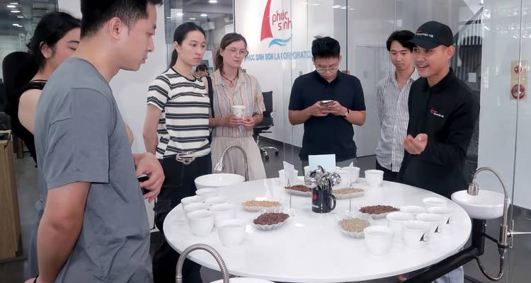 Visitors gathered around a tasting table with bowls of coffee beans inside a modern showroom.