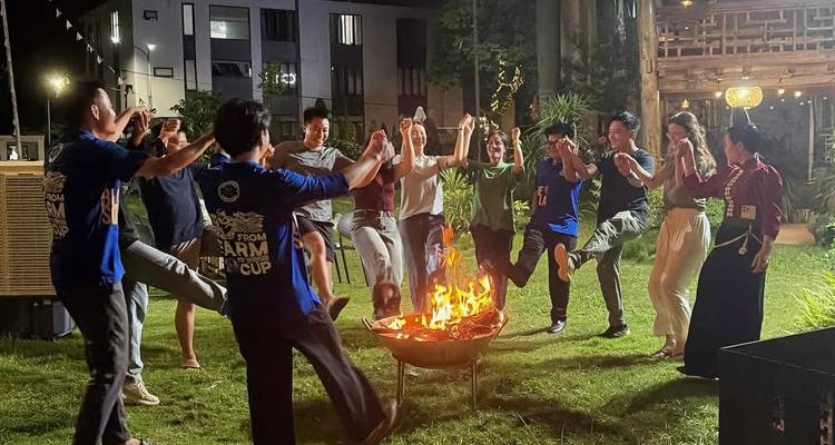 Group of travellers dancing in a circle around a campfire at night on grassy lawn.