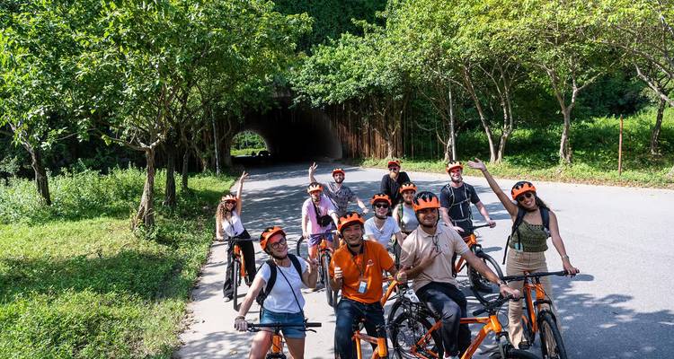 Cycling tour group wearing orange helmets posing on road near forested tunnel entrance.