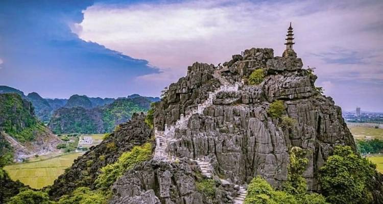 Dramatic limestone peak with zig-zag stone stairs leading to a small pagoda tower, panoramic valley below.