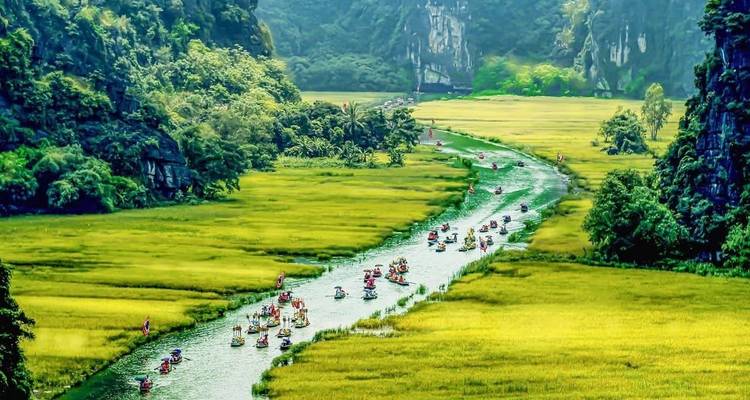 Boats with tourists glide along bright green rice valley river in dramatic karst scenery.