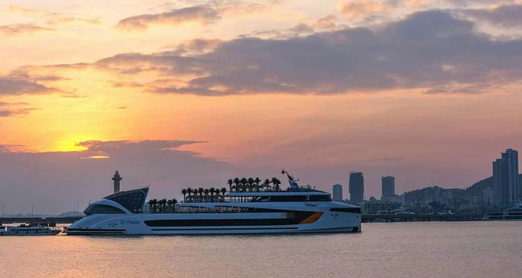 Sleek cruise ship silhouetted against orange sunset skyline near harbour.