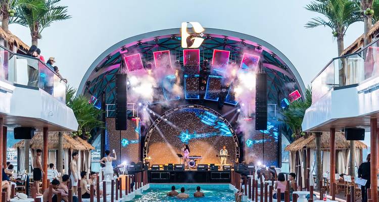 Nighttime pool party and live performance inside enclosed cruise deck with vibrant lights.
