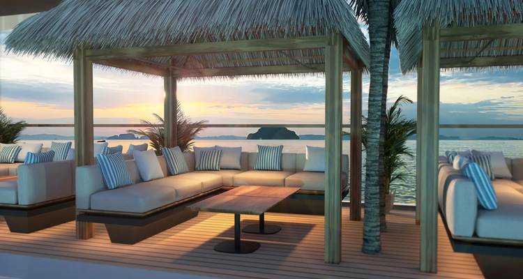 Comfortable cabana seating under thatched roof on deck overlooking tranquil sea at dusk.
