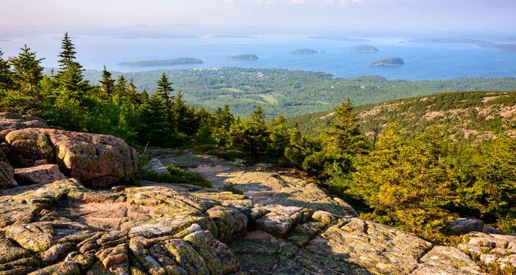 Granite summit view from Cadillac Mountain with rocky foreground overlooking islands scattered in blue Frenchman Bay.