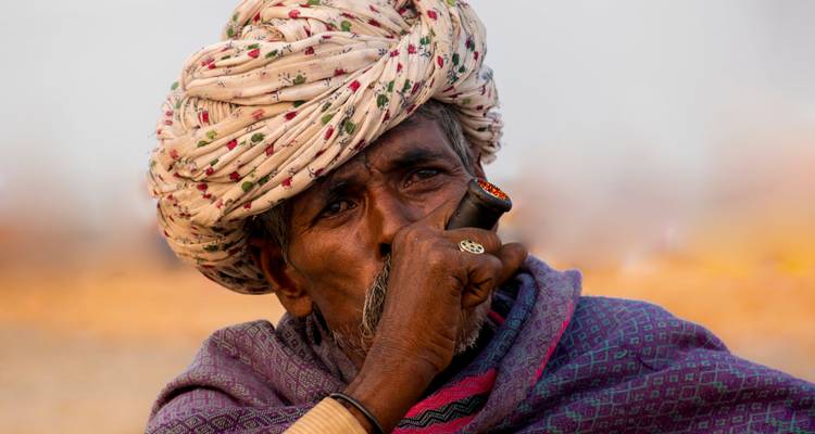 Dicht portret van een man uit Rajasthan in een gebloemde tulband die een traditionele pijp rookt.