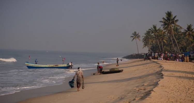 Early morning scene of fishermen and locals on a wide sandy beach with palm trees and a small boat
