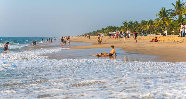 Sunny beach with vacationers playing in gentle waves and relaxing on golden sand lined by palm trees
