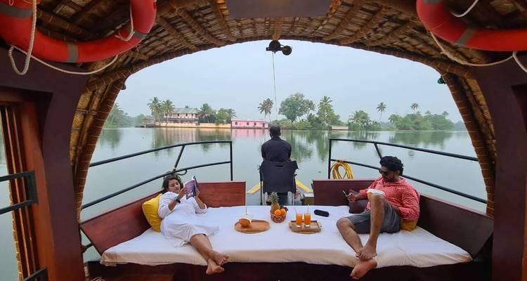 Couple lounging on a comfy daybed aboard a traditional Kerala houseboat cruising quiet backwaters