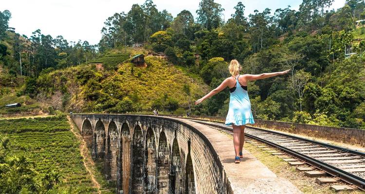 Woman balances on railway track atop the Nine Arches Bridge spanning a lush jungle valley.