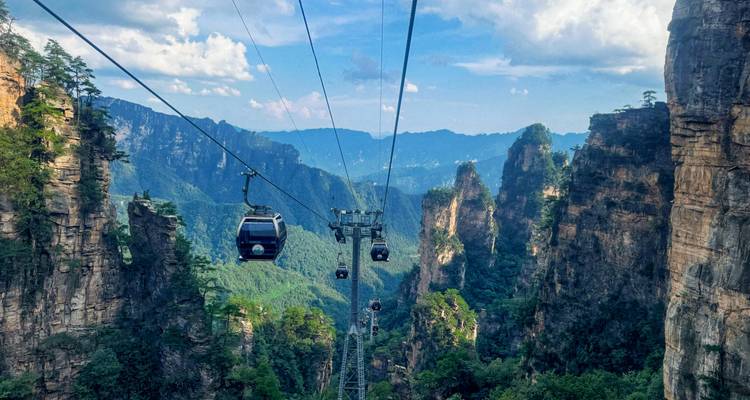 Des téléphériques en gondole glissant entre des falaises de grès à pic dans une vallée montagne luxuriante