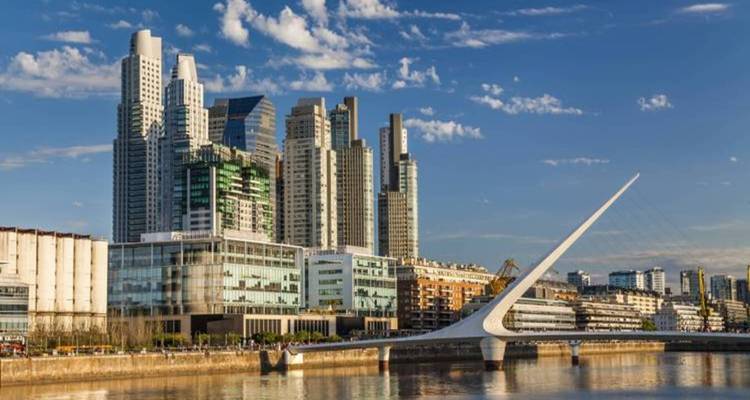 Modern skyscrapers of Puerto Madero and the white Puente de la Mujer span the docklands at golden hour.