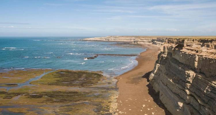 Dramatic coastline with tall stratified cliffs and teal ocean waters at low tide.