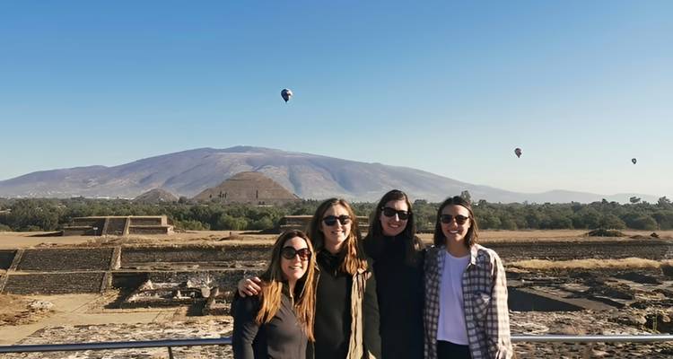 Gruppe von Freunden, die mit Heißluftballons und den Pyramiden von Teotihuacán gegen einen klaren blauen Himmel posieren.
