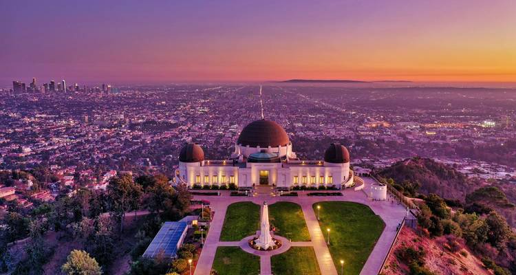 A spectacular aerial view of Griffith Observatory glowing at sunset above the sprawling city lights of Los Angeles.