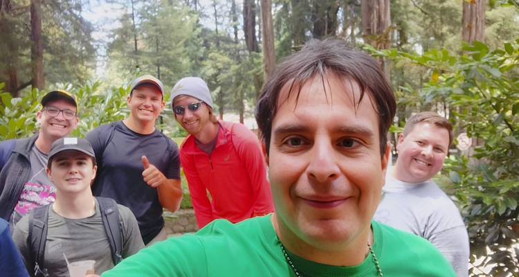 Eine lächelnde Gruppe macht ein Selfie auf einer sonnigen Waldlichtung während einer Wanderung.