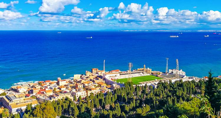 Panoramic view over Algiers’ coastal district, stadium, and deep blue Mediterranean Sea under scattered clouds.
