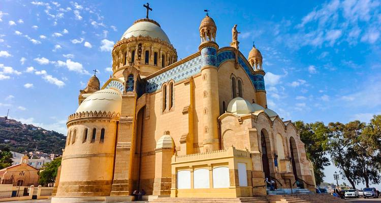 The ornate domes and mosaics of Notre-Dame d’Afrique basilica stand under a bright blue sky.