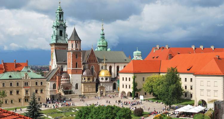 Panoramic aerial view of Wawel Cathedral and the surrounding red-roofed historic buildings in Krakow with crowds in the square.