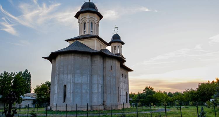 Small Orthodox church with twin towers standing in a grassy field at dusk with pastel colors in the evening sky.
