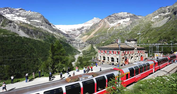 Der rote Bernina Express-Zug fährt in einen Bergbahnhof inmitten imposanter schneebedeckter Gipfel ein.