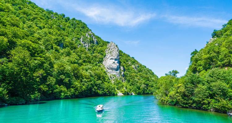 Turquoise river winding through lush canyon walls with a lone motorboat cruising below a jagged rock spire.