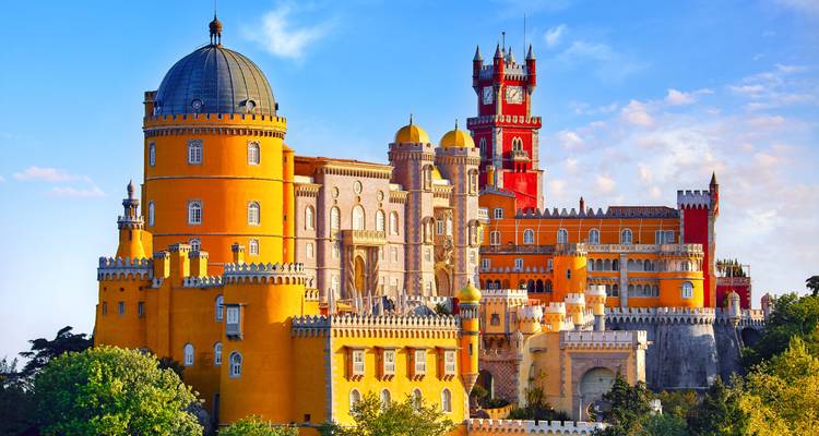 Vibrant yellow and red towers of Pena Palace rise above lush forest in Sintra against a bright blue sky.