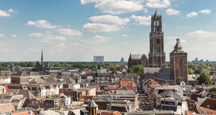 Aerial view over Utrecht’s red-tiled roofs dominated by the Dom Tower under fluffy clouds.