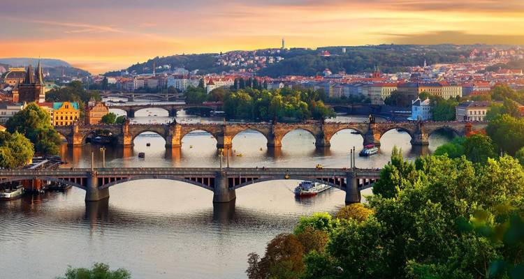 Multiple historic bridges span the Vltava River with Prague’s sunset skyline in the background.
