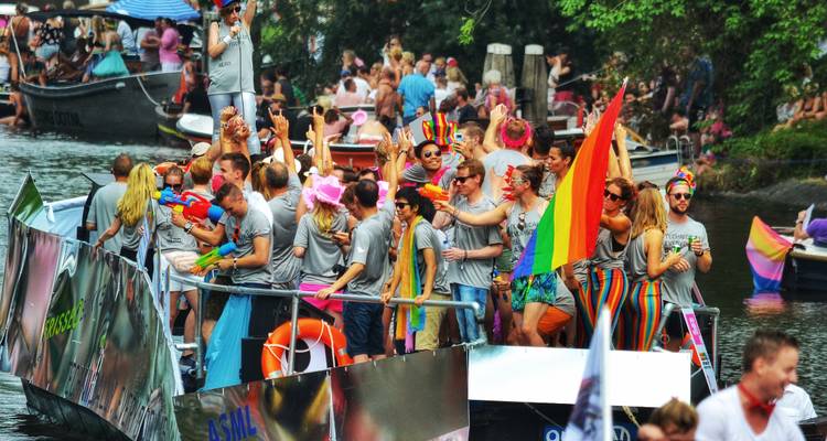Colorful pride boat parade crowded with people celebrating on Amsterdam’s canal