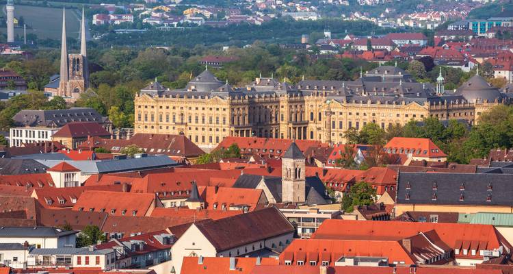 Elevated cityscape of red-roofed old town with an imposing baroque palace surrounded by greenery in the background