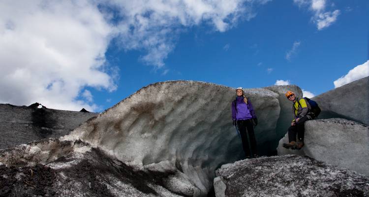 Les trekkeurs souriants se tiennent devant un mur de glace festonné sous un ciel bleu éclatant sur un glacier.