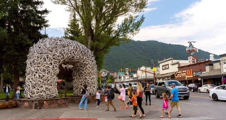 Visitors cross the famous antler arch in Jackson Hole town square with mountain backdrop and shops nearby.