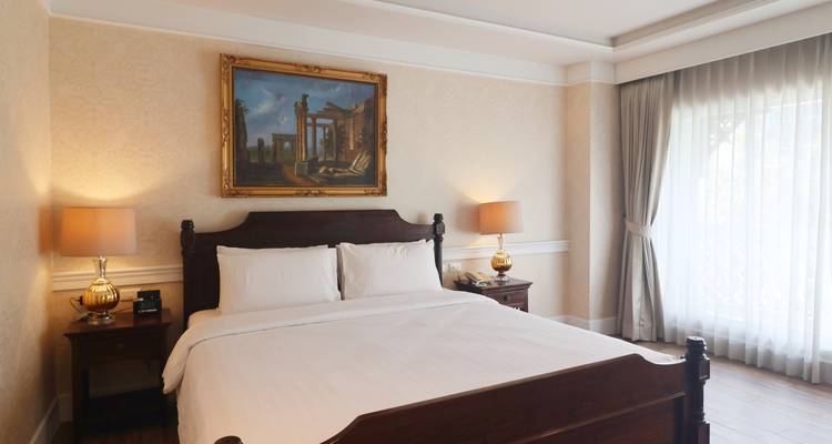 Klassisches Hotelzimmer mit gerahmtem Gemälde, eleganten Lampen und feinen Vorhängen, die sanftes Licht hereinlassen.